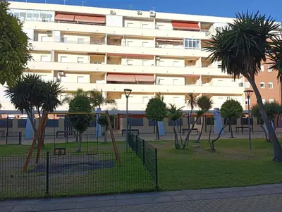 a building with a park with palm trees in front of it at Apartamento Vallehermoso in El Puerto de Santa María