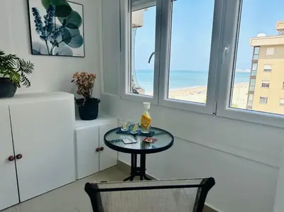 a table and a chair in a room with windows at Apartamento a pie de playa. in Cádiz