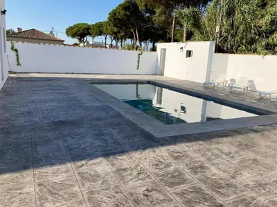 a swimming pool with chairs and a white wall at Villa El Lagar in Novo Sancti Petri