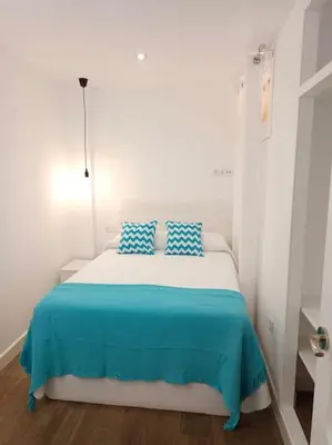 a white room with a bed with blue pillows at Fernando de Magallanes 15, Bajo en segunda línea de playa in Sanlúcar de Barrameda