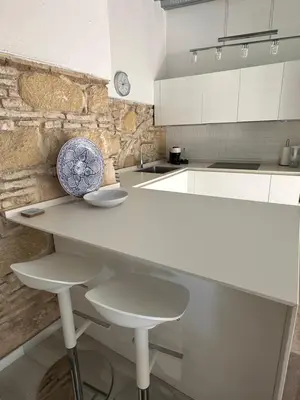 a white kitchen with a counter and stools at Casa Nuna Modern Loft with Private Garden Terrace in Jerez de la Frontera