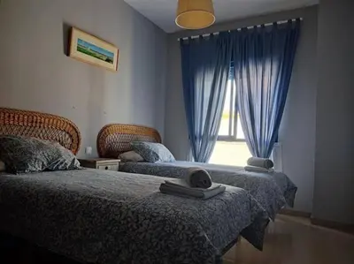 a bedroom with two beds and a window with blue curtains at AMPLIO PISO EN COSTA BALLENA A 100 M DE LA PLAYA in Costa Ballena