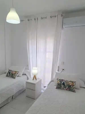 a white bedroom with two beds and a lamp at Dúplex en primera línea de playa 15 in Sanlúcar de Barrameda