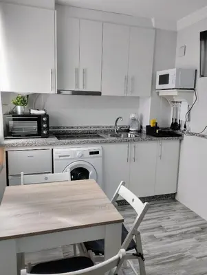 a kitchen with white cabinets and a table with a chair at Apartamento Puertomar in El Puerto de Santa María