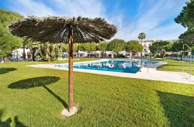 an umbrella in the grass next to a swimming pool at Carrajolilla Sancti petri in Chiclana de la Frontera