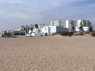 a sandy beach with buildings in the background at Apto. en la playa del parque natural los Turuños in El Puerto de Santa María
