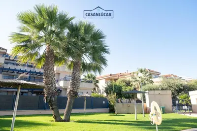 two palm trees in a park in front of a building at Vivienda Magallanes in Sanlúcar de Barrameda