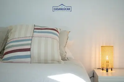 a white bed with a pillow and a lamp at Vivienda Magallanes in Sanlúcar de Barrameda