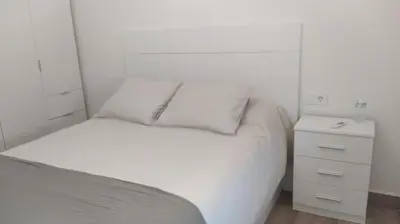 a white bedroom with a bed and a night stand at Casa Ángeles in Cádiz