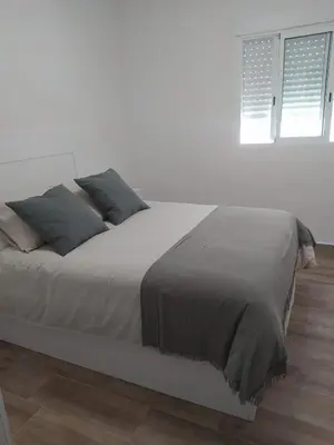 a white bedroom with a large bed with blue pillows at Casa Ángeles in Cádiz