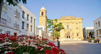 a building with a clock tower and flowers in front of it at Apartamento Costa de Sancti Petri by Chiclana Dreams in Novo Sancti Petri