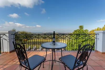a table with two chairs and a bottle of wine on a balcony at Arcos Gardens Sol Rent Golf in Arcos de la Frontera
