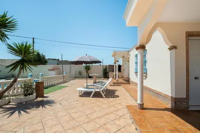 a patio with chairs and an umbrella on a house at El Verano Azul Casa con piscina in Chiclana de la Frontera