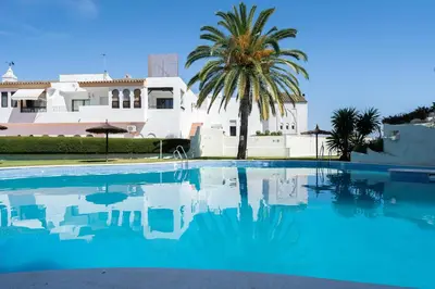 a swimming pool with a palm tree and a house at Apartoyou - Vistahermosa Bahía in El Puerto de Santa María
