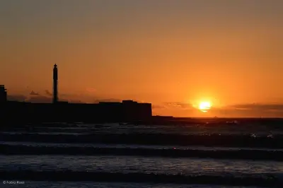 a sunset on the beach with a lighthouse in the background at Aire del Sur Cádiz in Cádiz
