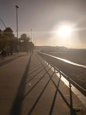 a shadow of a person walking on a sidewalk next to the beach at PLAYA LAS PILETAS-CALZADA in Sanlúcar de Barrameda