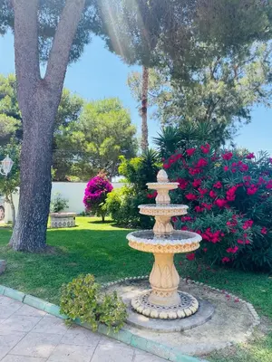 a stone fountain in a park with pink flowers at Brisa Home in Chiclana de la Frontera