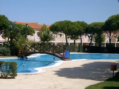 a bridge over a swimming pool with trees and buildings at Chiclana.Balconera.1ªlínea playa in Chiclana de la Frontera