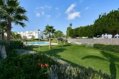 a garden with a swimming pool and palm trees at Acogedora vivienda Costa Ballena in Chipiona