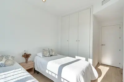 a white bedroom with two beds and a mirror at Acogedora vivienda Costa Ballena in Chipiona