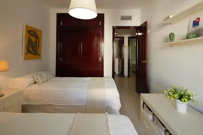 a bedroom with two beds and a table with flowers at Paso del Mar Ha Apartment in Cádiz