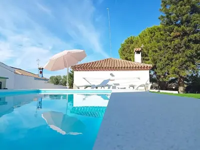a swimming pool with an umbrella and a house at Casa de campo con piscina in Chiclana de la Frontera