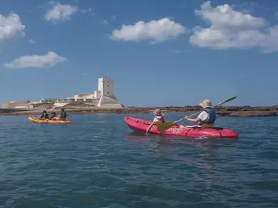 three people kayaking on the water with a lighthouse in the background at PuraVidaChiclana in Chiclana de la Frontera