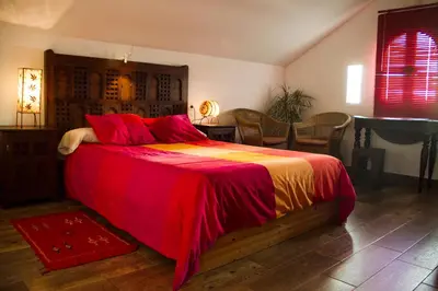 a bedroom with a bed with a red and orange blanket at El Fogón del Duende in Arcos de la Frontera