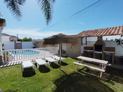 a yard with benches and an umbrella and a swimming pool at Casa Ramos in Conil de la Frontera