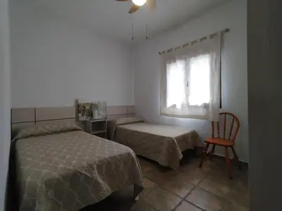 a bedroom with two beds and a chair and a window at Casa Ramos in Conil de la Frontera