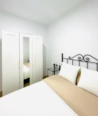 a white bedroom with a bed and a mirror at Apartamento Merykuki in Sanlúcar de Barrameda