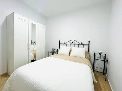 a white bedroom with a white bed and a mirror at Apartamento Merykuki in Sanlúcar de Barrameda