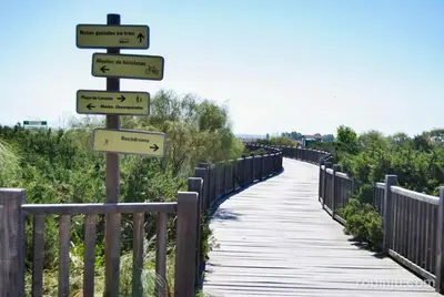 a wooden boardwalk with signs pointing to different directions at Apartamento Las Olas de Valdelagrana in El Puerto de Santa María
