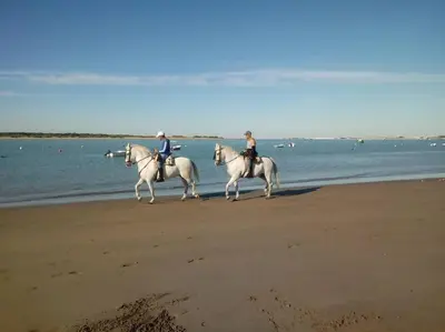 two people are riding horses on the beach at La Carabela, Elcano in Sanlúcar de Barrameda