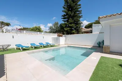 a swimming pool with blue chairs in a backyard at La Perla Costera in Chiclana de la Frontera