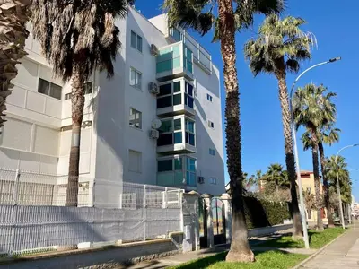 a white building with palm trees in front of it at APARTAMENTO SALINAS VALDELAGRANA - WiFi, Playa, Piscina in El Puerto de Santa María