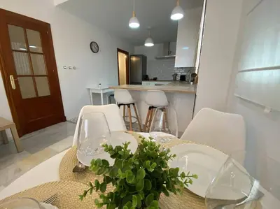 a dining room table with white chairs and a table with a plant at Apartamento en centro con garaje in Sanlúcar de Barrameda