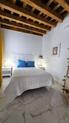 a white bedroom with a large bed with blue pillows at Don Roman Suites en pleno centro by Sanlúcar Housing in Sanlúcar de Barrameda