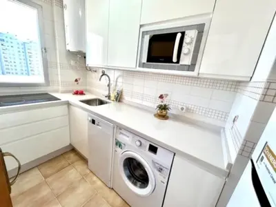 a white kitchen with a washing machine and a microwave at GATU DULCE junto playa, terraza, aire acc, parking, piscina , 
