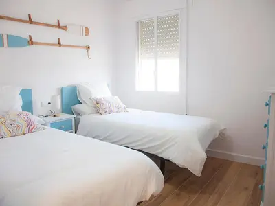 two beds in a white room with a window at Sanlucarsun Apartamento frente al mar in Sanlúcar de Barrameda