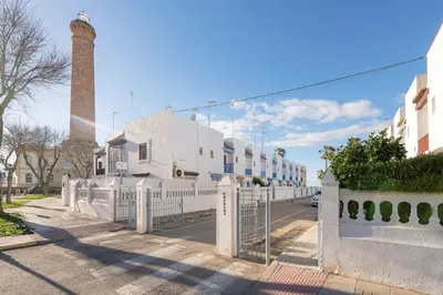 a white fence in front of a building with a tower at El Paseo del Faro in Chipiona