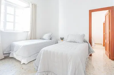 a white bedroom with two beds and a window at Carril San Diego, junto a la Plaza Cabildo in Sanlúcar de Barrameda