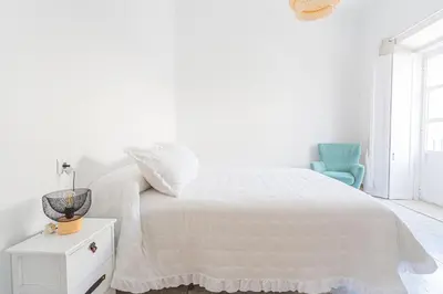 a white bedroom with a bed and a blue chair at Carril San Diego, junto a la Plaza Cabildo in Sanlúcar de Barrameda