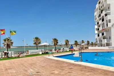a swimming pool in front of a building and the ocean at Valdelagrana Marinero in El Puerto de Santa María