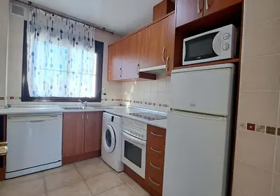 a kitchen with white appliances and wooden cabinets at Segunda planta con terraza y solarium in Chiclana de la Frontera