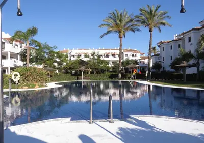 a large swimming pool with palm trees and buildings at Segunda planta con terraza y solarium in Chiclana de la Frontera