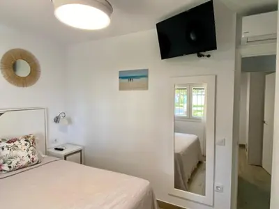 a bedroom with two beds and a tv on the wall at Moderno Apartamento Primera Línea Playa de La Barrosa by ChiclanaDreams in Chiclana de la Frontera