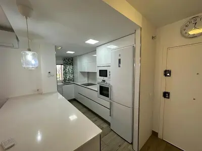 a kitchen with white cabinets and a clock on the wall at Moderno Apartamento Primera Línea Playa de La Barrosa by ChiclanaDreams in Chiclana de la Frontera