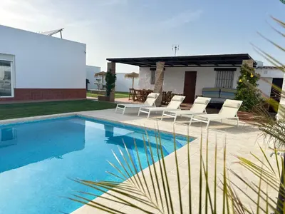 a swimming pool with white chairs and a house at Villa Luna Novo Santi Petri in Chiclana de la Frontera