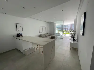 a white kitchen with a table and a living room at Costa Ballena - Dos dormitorios, Piscina y Jardín privado in Cádiz
